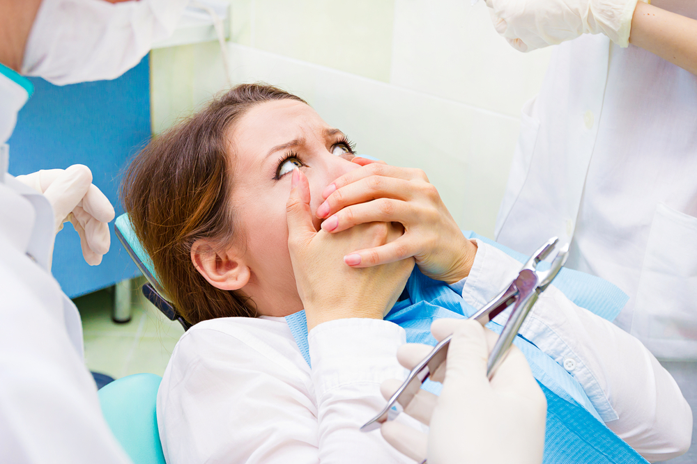 Closeup portrait young terrified girl woman scared at dentist visit, siting in chair, covering her mouth, doesnt want dental procedure, drilling, tooth extraction, isolated clinic office background